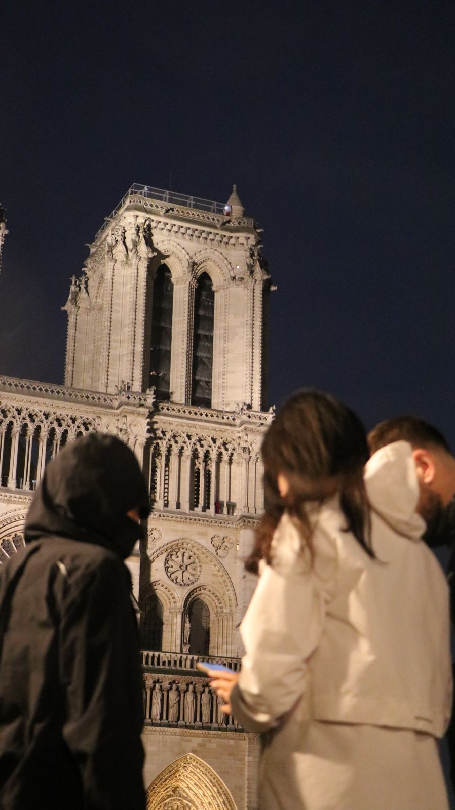 Des joueurs devant Notre-Dame de Paris à la tombée de la nuit, téléphone à la main.